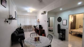 A living room with a sofa, a dining table with chairs, a TV, and a kitchen area with a fridge.