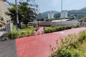 A paved walkway with greenery, a building in the background, and a clear sky. - Permai Ria Home Apartment (Tanjung Bungah)