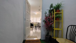 A hallway with a welcome mat, a yellow plant stand, and a chair. - Permai Ria Home Apartment (Tanjung Bungah)