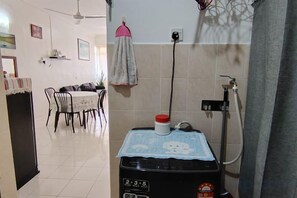 A kitchen with a water dispenser, a dining area with chairs and a table, and a tiled floor. - Permai Ria Home Apartment (Tanjung Bungah)