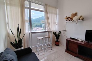 A living room with a sofa, a TV stand, a window with curtains, and a plant. - Permai Ria Home Apartment (Tanjung Bungah)