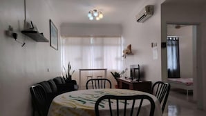 A dining area with a table set for four, a TV, and a dog on a shelf. - Permai Ria Home Apartment (Tanjung Bungah)