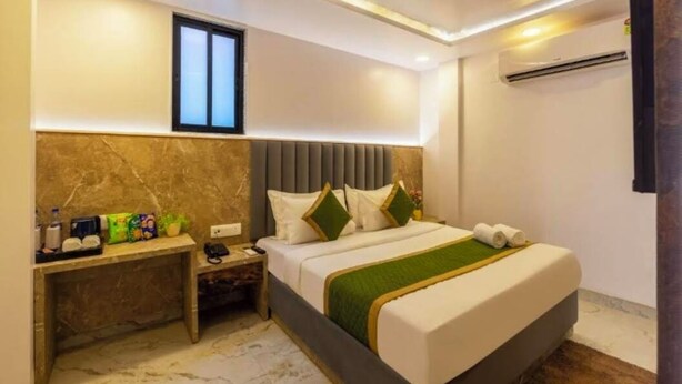 A modern hotel room with a marble floor, a bed with a green throw, a nightstand with a phone and a lamp, and a window with blinds. - Hotel Rachna Tourist lodge  (New Delhi)