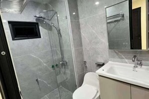Une salle de bain moderne avec une douche à parois de verre, des toilettes blanches et un lavabo surmonté d’un miroir.