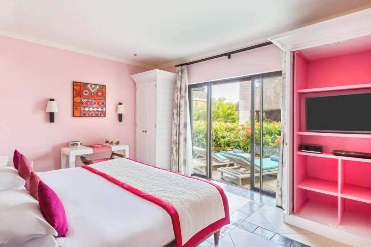 A bedroom with a bed, a TV, a sliding glass door to a balcony, and a pink shelving unit.