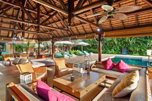 A covered outdoor lounge area with seating and a pool in the background. - Club Med Albion Villas (Mauritius)