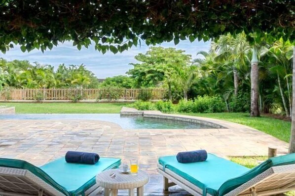 A poolside area with lounge chairs and a small table, surrounded by lush greenery and a wooden fence. - Club Med Albion Villas (Mauritius)