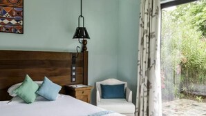 A bedroom with a wooden headboard, a bed with pillows, a nightstand, a chair, and a window with curtains. - Club Med Albion Villas (Mauritius)