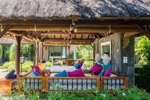 A covered outdoor seating area with cushioned benches and colorful pillows, surrounded by lush greenery. - Club Med Albion Villas (Mauritius)