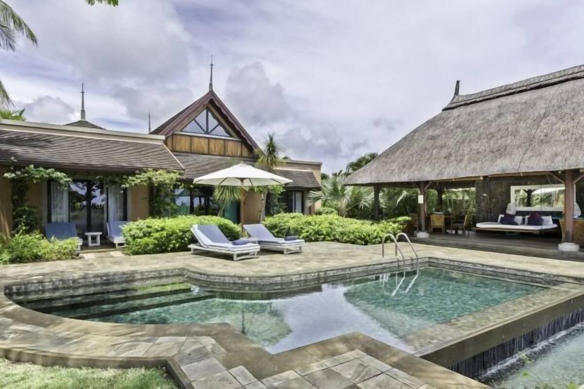 A pool area with lounge chairs, a thatched-roof structure, and a wooden building with a sloped roof.
