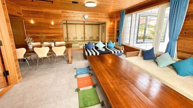 A wooden interior with a long dining table, cushioned seating, and large windows. - Base Shiraoi (Shiraoi)