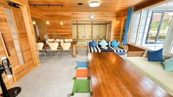 A wooden interior with a long dining table, chairs, and a sofa with cushions.