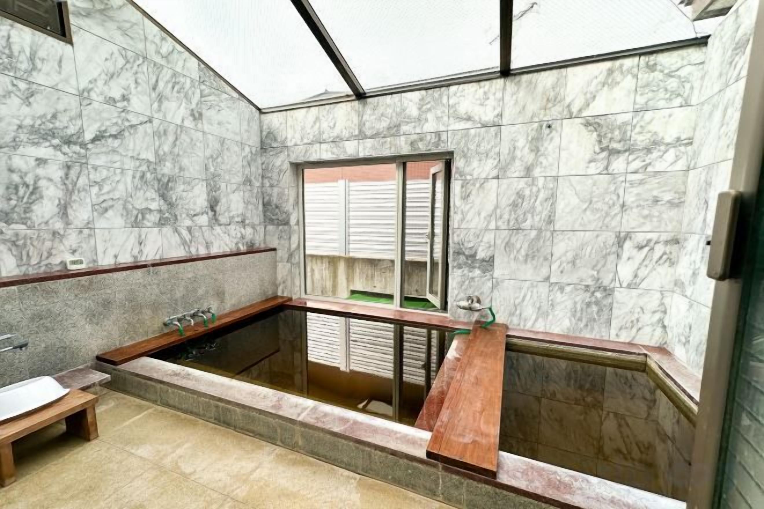 A bathroom with a marble wall, a bathtub, and a window.