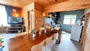 A wooden interior with a dining table, chairs, a TV, and a kitchen area. - Base Shiraoi (Shiraoi)