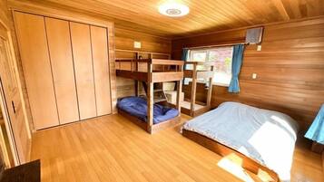 A wooden-floored room with bunk beds, a wardrobe, and a television.