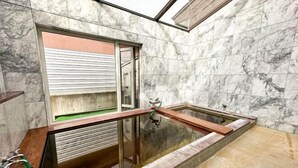 A modern bathroom with marble walls, a glass-enclosed shower, and a wooden bench. - Base Shiraoi (Shiraoi)