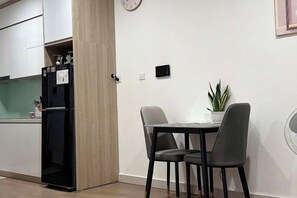 A compact kitchen with a refrigerator, a dining table with two chairs, and a potted plant. - Homestay Nha Thu Thu (Hanoi)