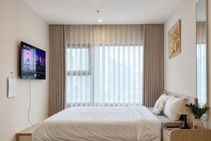 A hotel room with a large bed, a television mounted on the wall, a window with curtains, and a bedside table with a lamp and a plant. - Homestay Nha Thu Thu (Hanoi)