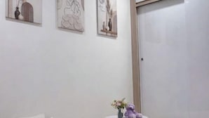 Una stanza con un muro bianco, un tavolo rotondo con un vaso e un orsacchiotto, e tre opere d'arte incorniciate sopra il tavolo.