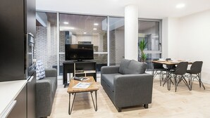 A modern living room with a grey sofa, a coffee table, a TV, and a dining area with a table and chairs. - Dominick Place (Dublin)