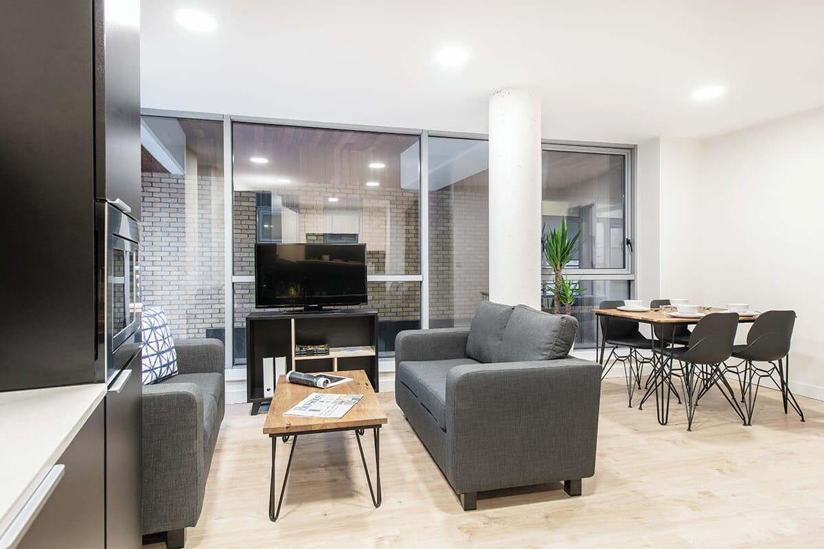 A modern living room with a grey sofa, a coffee table, a TV, and a dining area with a table and chairs.