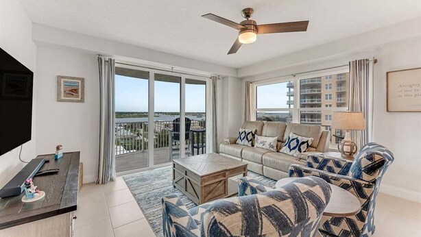 A spacious living room with a large sofa, armchairs, a coffee table, and a ceiling fan.