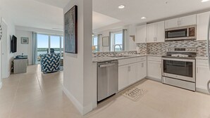 A modern kitchen with white cabinets, a microwave, an oven, and a dishwasher. There is a large window and a view of the outdoors.