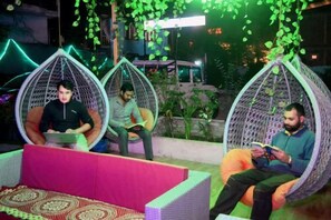 Three individuals seated in hanging chairs with a patterned floor and a neon sign in the background. - Dream Valley Kasol (Kasol)