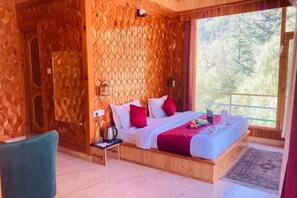 A wooden room with a bed, a chair, a nightstand, and a window with a view of trees. - Dream Valley Kasol (Kasol)