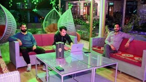 A modern lounge area with wicker furniture, a glass coffee table, and a laptop on the table. - Dream Valley Kasol (Kasol)