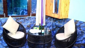 Three wicker chairs with cushions, a small table with bottles and glasses, and a tiled floor. - Dream Valley Kasol (Kasol)