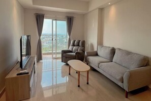 A modern living room with a sofa, a coffee table, and a TV on a wooden stand. - 3BR Podomoro Apartment @Empire Tower 107 sqm² (Kesawan)