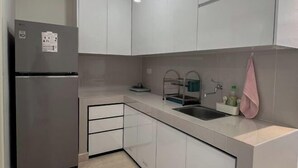 A modern kitchen with white cabinets, a stainless steel refrigerator, a sink, and a pink towel hanging on the wall. - 3BR Podomoro Apartment @Empire Tower 107 sqm² (Kesawan)