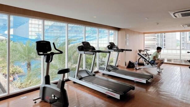 A gym with treadmills and an elliptical machine, large windows, and a view of greenery outside. - 3BR Podomoro Apartment @Empire Tower 107 sqm² (Kesawan)