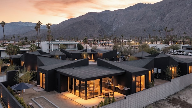 Un hôtel moderne composé de plusieurs bâtiments aux toits noirs, doté d’un vaste patio et offrant une vue sur les montagnes.