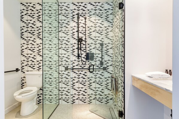 Une salle de bain avec une douche à parois de verre, des toilettes et un plan de toilette en marbre agrémenté d’articles de toilette.