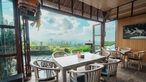 Un comedor con una mesa y sillas, ventanas amplias con vista a un paisaje verde, y un cuadro en la pared.