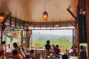 Un comedor interior con mesas y sillas, techo de madera y vistas al exterior.