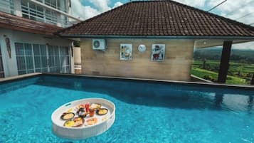 Una piscina con una bandeja de comida flotando, un edificio con tejado de baldosas y vistas a un paisaje verde.