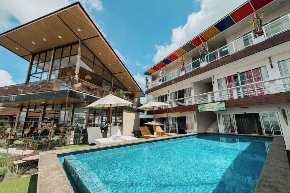 A hotel with a swimming pool, outdoor seating, and a multi-story building with balconies.