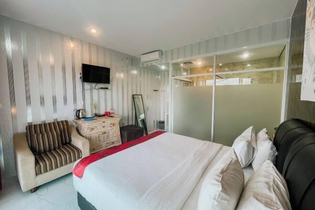 A hotel room with a bed, a sofa, a TV, a dresser, and a sliding glass door leading to a balcony.