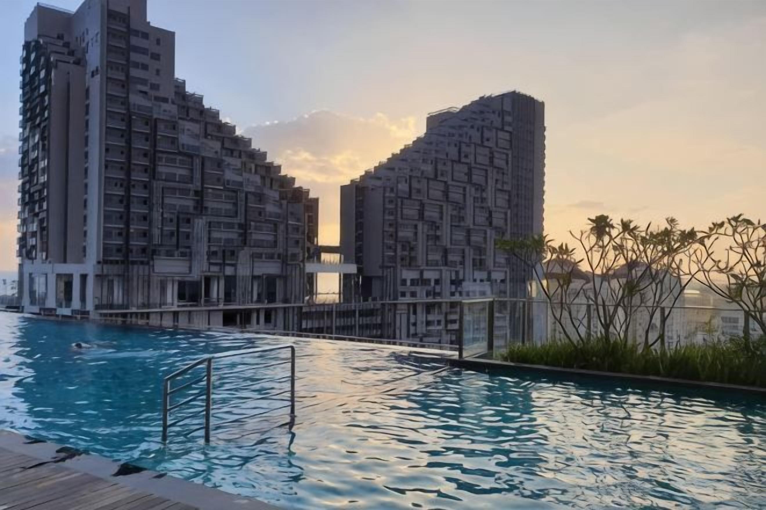 A swimming pool with a wooden deck, surrounded by high-rise buildings.