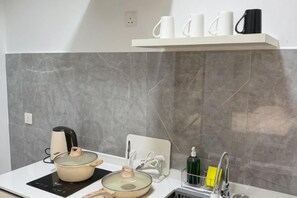 A kitchen with a white countertop, a pot, a kettle, a coffee maker, and a shelf with cups.