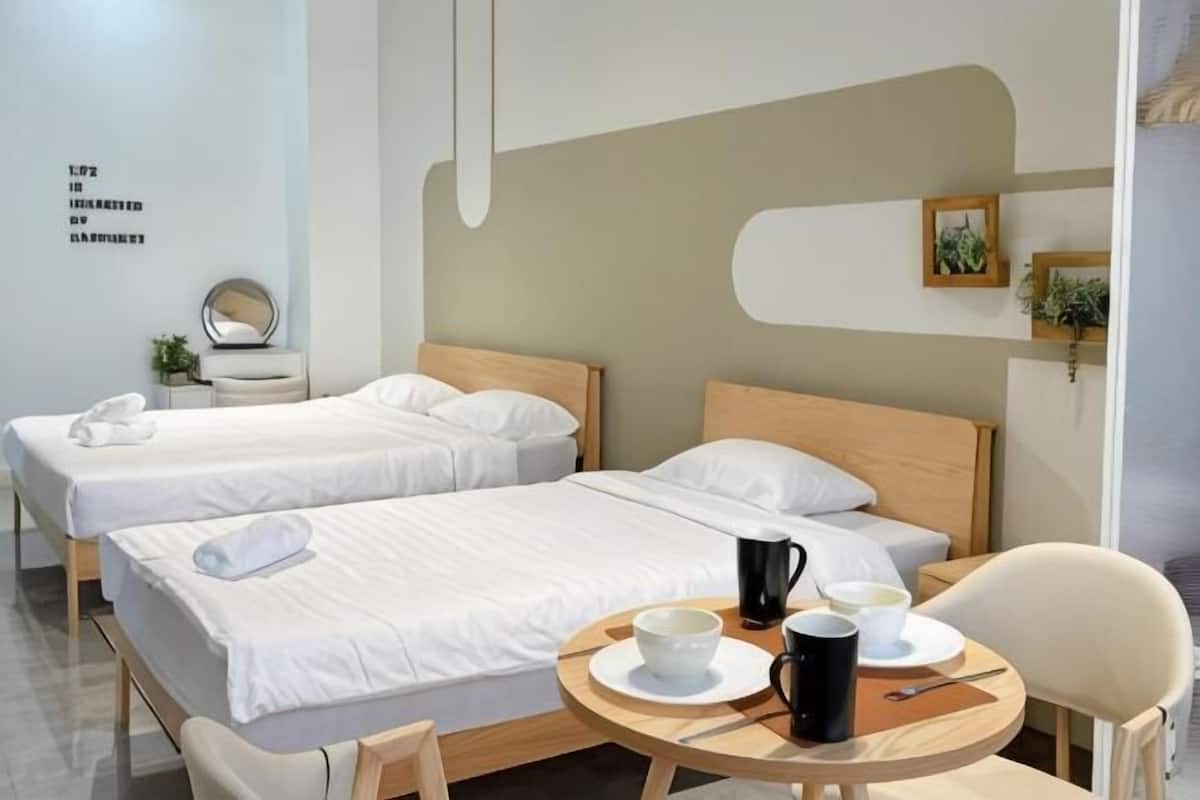 Une chambre d’hôtel avec deux lits, une table ronde, une cafetière, des tasses et une chaise.