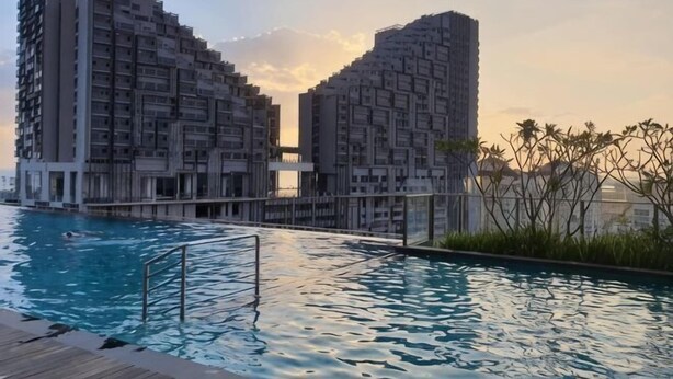 A swimming pool with a wooden deck, surrounded by high-rise buildings with a unique architectural design. - Imperio Melaka by Iconique (Melaka)