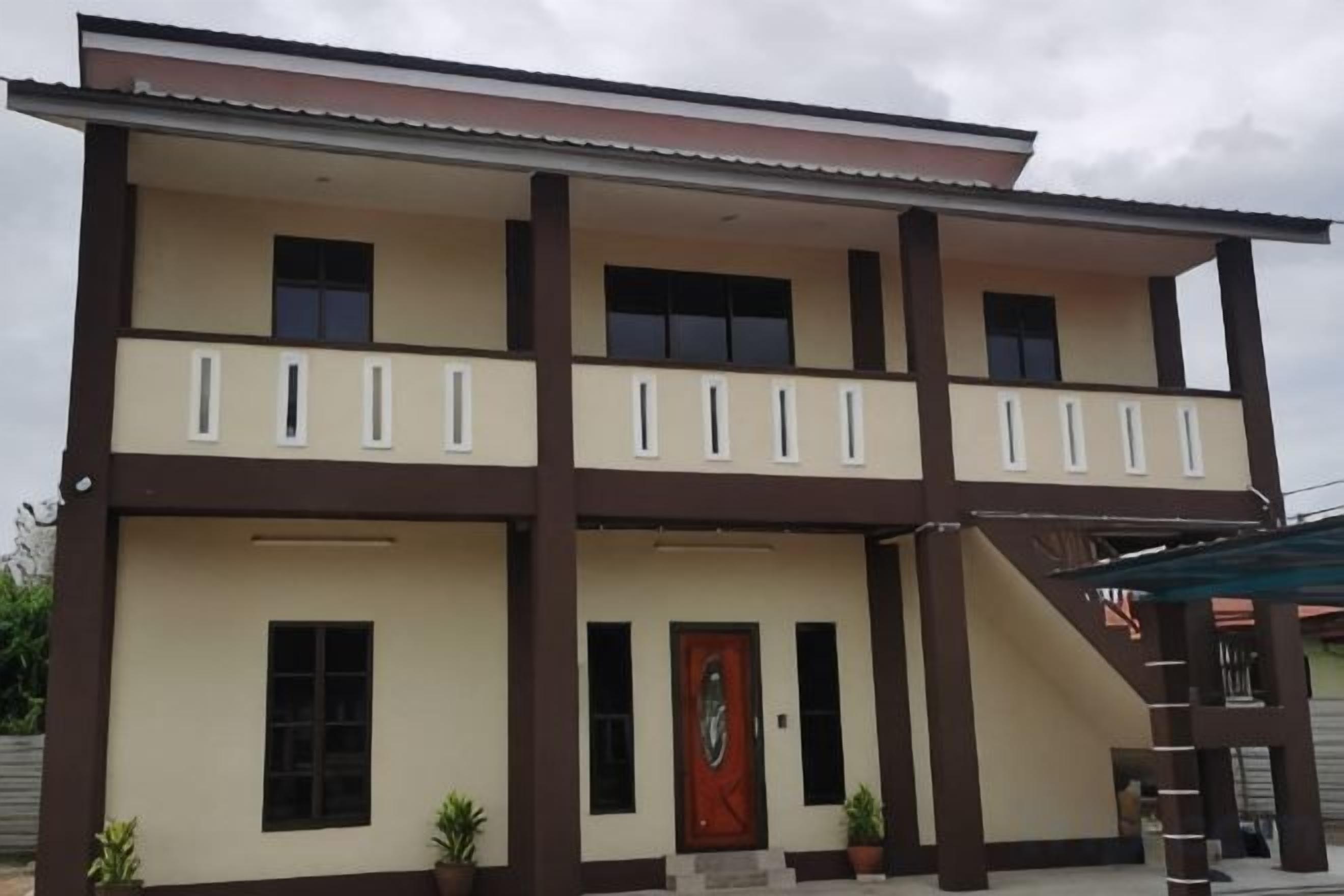 A two-story building with a balcony on the upper floor, a red door, and a covered entrance area.