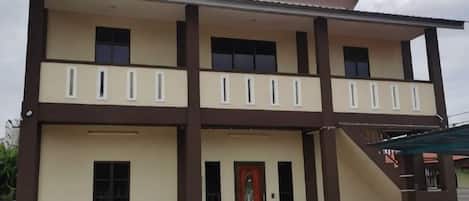 A two-story building with a balcony on the upper floor, a red door, and a covered entrance area.