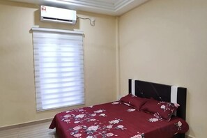 A bedroom with a bed, a window with blinds, and an air conditioning unit. - Villa Tok Wan (Kuala Kuantan)