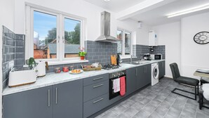 Una cocina moderna con armarios grises, horno empotrado, microondas y ventana con vista a una casa.