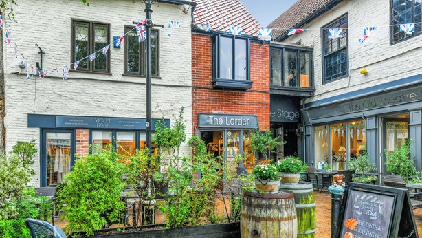 Un pub tradicional con mesas al aire libre, un letrero que dice 'The Larder' y una pancarta que anuncia 'The Old Theatre'.